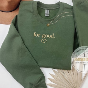 May include: A green sweatshirt with the text "for good." embroidered in gold on the front. The sweatshirt has a heart symbol below the text.