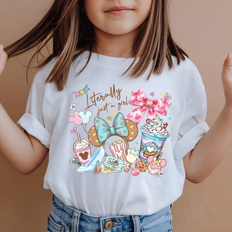 May include: White t-shirt with a colorful graphic design featuring a bow, Mickey Mouse ears, a high heel, popcorn, and a drink. The text "Literally just a girl" is written in script across the top of the design.