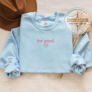 May include: Light blue sweatshirt with the text "for good." embroidered in pink with a small pink heart below the text.