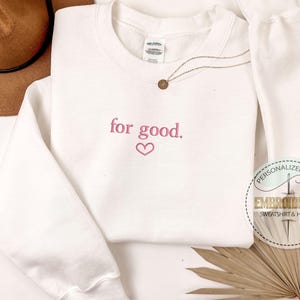 May include: White sweatshirt with the text "for good." embroidered in pink with a pink heart below the text.
