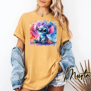 May include: Mustard-coloured t-shirt featuring a watercolour image of Stitch from Lilo & Stitch. The graphic shows Stitch in shades of blue, with a colourful background. The word "Mustard" is written in a script font.