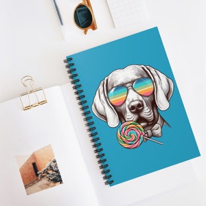 May include: A white dog with rainbow sunglasses and a bow tie is holding a colorful lollipop. The dog is on a blue background.