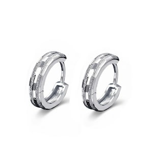 May include: Two silver hoop earrings with a geometric design. The earrings have a series of rectangular and square shapes, with a mix of shiny and textured surfaces. The earrings are displayed against a white background.