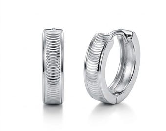 Peut inclure: Une paire de créoles argentées avec une finition polie et une bande centrale ornée d'une texture nervurée verticale répétitive. Les boucles d'oreilles présentent un mécanisme de fermeture à charnière et une forme circulaire lisse et brillante.