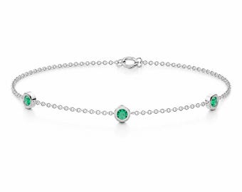May include: A delicate silver chain bracelet featuring three round, bezel-set green gemstones spaced evenly along the length. The bracelet includes a small circular clasp mechanism at the top centre, connecting the two ends of the fine metal chain.