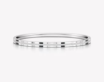May include: A thin silver-toned bangle bracelet featuring a repeating pattern of alternating smooth metallic segments and textured, glittery rectangular sections that wrap around the entire circumference of the circular band.