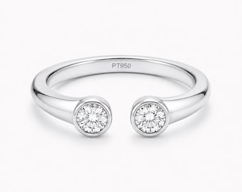 Può includere: Un anello aperto color argento con due pietre rotonde, chiare e sfaccettate, incastonate a lunetta su ciascuna estremità. La fascia interna presenta l'incisione PT950, che indica la composizione in platino di questo gioiello.