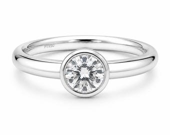 Può includere: Un anello in platino con un diamante rotondo a taglio brillante incastonato in una montatura a lunetta liscia. L'interno della fascia lucida presenta l'incisione PT950, che indica la composizione metallica di questo gioiello circolare.