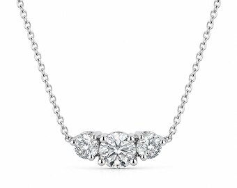 Può includere: Una collana color argento con un ciondolo centrale composto da tre pietre rotonde, trasparenti e sfaccettate disposte orizzontalmente. Il ciondolo è fissato a una sottile e delicata catena metallica con maglie circolari uniformi.