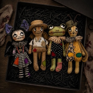 May include: Four handcrafted fabric dolls with stitched facial features and button accents. The dolls include a bat-like figure, a turtle-like character in a straw hat, a green frog-like creature, and a bug-like doll wearing a small green hat.