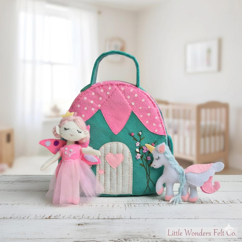 Pu&ograve; includere: Una bambola fata in feltro con ali rosa e gonna in tulle &egrave; accanto a una borsa in feltro a forma di casa con manico. &Egrave; presente anche un unicorno in feltro con criniera blu e dettagli rosa. La borsa &egrave; verde acqua e rosa.