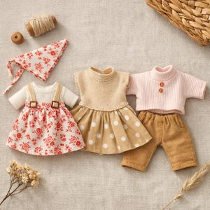 May include: A collection of miniature doll clothes, including a floral print dress, a polka dot dress, a pink sweater, and brown pants. Accessories include a matching bandana and a spool of thread.
