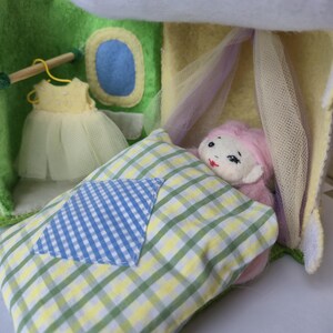 May include: A felt dollhouse with a doll sleeping on a checkered pillow under a sheer canopy. A yellow dress hangs in the dollhouse closet. The doll has pink hair and a painted face. The dollhouse is green and yellow.