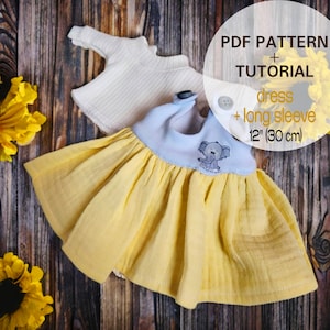 以下が含まれることがあります： 12インチ（30cm）のドールドレスと長袖のPDFパターンとチュートリアル。ドレスは黄色で、青いボディスと刺繍されたゾウが付いています。長袖は白です。