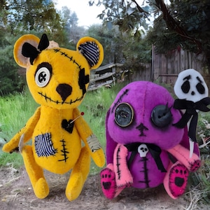 May include: Two handmade plush toys: a yellow bear with black stitches and a purple bunny with button eyes. The bear has a heart patch and the bunny holds a skull lollipop. Both have a stitched, slightly spooky aesthetic.