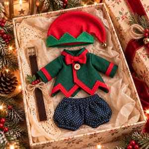 May include: A doll clothing set featuring a red felt hat with a green trim and a small bell, a dark green felt jacket with red trim, a red bow tie, and a wooden button, and dark blue shorts with a white polka dot pattern, all inside a gift box.