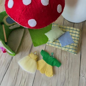 May include: A collection of handmade felt toys, including a red mushroom with white spots, a green felt chair, a yellow dress, and a green and yellow flower. Also included are a green pillow and a plaid pillow.