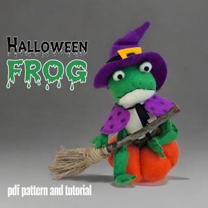 May include: A felt Halloween frog wearing a purple witch hat and cape, holding a broom, and sitting on an orange pumpkin. The image includes the text "HALLOWEEN FROG" and "pdf pattern and tutorial".