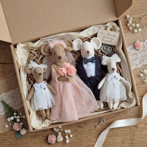 Könnte beinhalten: Eine Hochzeits-Andenkenbox mit vier Mäusepuppen, die für eine Hochzeit gekleidet sind. Die Brautmaus trägt ein rosa Kleid und Schleier und hält einen Blumenstrauß. Die Bräutigammaus trägt einen Smoking. Die Box enthält ein Etikett mit der Aufschrift "Our Family Wedding Keepsake" und ein Paar Ringe.