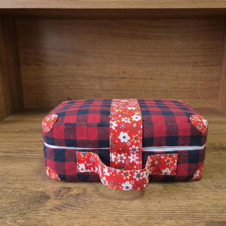 Peut inclure: Petite bo&icirc;te rectangulaire en tissu &agrave; motif de carreaux rouges et noirs. Une sangle &agrave; motifs floraux entoure la bo&icirc;te, et une poign&eacute;e assortie est attach&eacute;e. La bo&icirc;te mesure environ 15 cm de long, 10 cm de large et 8 cm de haut.