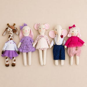May include: A collection of five fabric animal dolls including a giraffe in a white top and purple skirt, a rabbit in a purple polka dot dress, a mouse in a floral outfit, an elephant in blue overalls, and a sheep in a pink top and striped trousers.