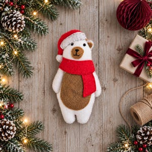 May include: A felt polar bear ornament featuring a white body with a brown belly, wearing a red scarf and a red Santa hat with a white trim. The bear has black bead eyes and a stitched brown nose, presented as a festive holiday decoration.