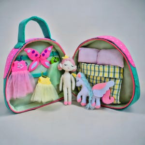Pu&ograve; includere: Una valigetta per bambole in tessuto rosa e verde, aperta per rivelare una bambola, vestiti, una farfalla e un unicorno. La valigetta ha un manico ed &egrave; decorata con pois rosa. All'interno ci sono una bambola, vestiti, una farfalla, un unicorno, cuscini e un letto.