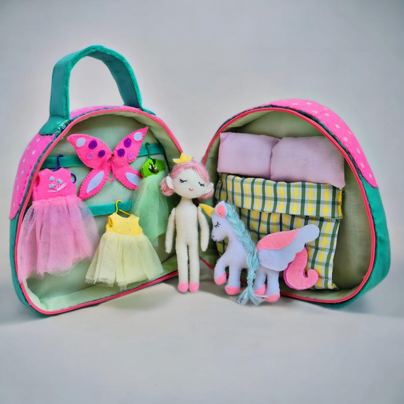 Pu&ograve; includere: Una valigetta per bambole in tessuto rosa e verde, aperta per rivelare una bambola, vestiti, una farfalla e un unicorno. La valigetta ha un manico ed &egrave; decorata con pois rosa. All'interno ci sono una bambola, vestiti, una farfalla, un unicorno, cuscini e un letto.