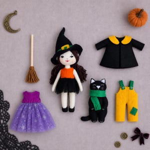 Può includere: Una bambola strega in feltro con capelli scuri e cappello nero, accompagnata da un gatto nero con sciarpa verde, una scopa, un vestito in tulle viola, un cappotto nero con colletto giallo, una salopette gialla, un ciondolo a mezzaluna e una zucca.