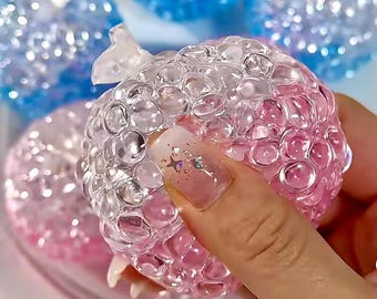 Op de afbeelding: Een doorzichtige, roze en witte squishy bal met een textuur. De bal is gemaakt van veel kleine bubbels.