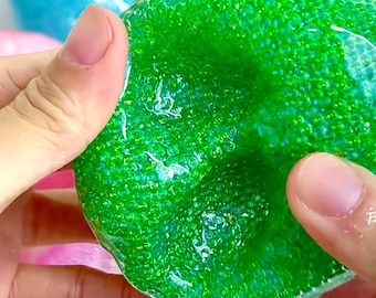 Op de afbeelding: Een verzameling kleurrijke, zachte ballen gevuld met kleine kralen. De ballen zijn doorschijnend en laten de kralen in het binnenste zien. De ballen zijn groen, blauw, roze en lichtblauw.