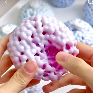 Peut inclure: Une balle moelleuse blanche et rose avec une surface texturée. La balle est faite de petites perles rondes qui sont reliées entre elles. L'intérieur de la balle est de couleur rose vif.