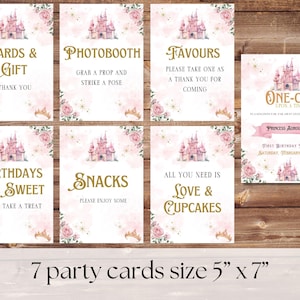 May include: Seven printable party cards featuring a pink castle and gold text. The cards are 5 inches by 7 inches and include the text "Cards & Gift", "Photobooth", "Favors", "Birthdays Are Sweet", "Snacks", "All You Need Is Love & Cupcakes", and "One-ce Upon A Time Princess Auroura First Birthday Party Saturday, February 8, 2015".