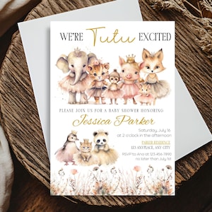 May include: A baby shower invitation with the text "WE'RE Tutu EXCITED" in gold script. The invitation features watercolor illustrations of animals wearing tutus and crowns. The invitation is on a white card, placed on a wooden surface.