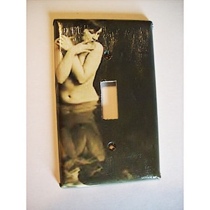 May include: A light switch cover with a vintage image of a woman in a flowing dress. The cover is dark green with a light switch cutout.