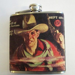 Könnte beinhalten: Hüftflasche aus Edelstahl mit einem Vintage-Western-Design. Das Bild auf der Flasche zeigt einen Cowboy mit einer Waffe, der einen Hut trägt, sowie den Text "The Thrill of Action" und "Sept 10". Die Flasche hat einen silbernen Verschluss und ein Scharnier.