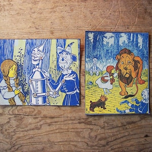 Könnte beinhalten: Zwei Vintage-Illustrationen aus dem Zauberer von Oz. Die erste zeigt den Blechmann, den Vogelscheuchen und Dorothy. Die zweite zeigt den Feigen Löwen, Dorothy und die böse Hexe des Westens.