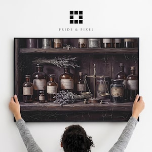 May include: A framed print of a vintage apothecary scene. The artwork shows dark brown glass bottles, jars, and a balance scale on a wooden shelf. Bundles of lavender and labels with text add detail. The print is held by a person.