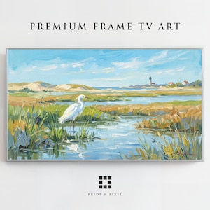 Può includere: Un dipinto paesaggistico intitolato PREMIUM FRAME TV ART raffigurante un'egretta bianca in una zona umida con erba alta, acqua blu e un faro in lontananza sotto un cielo luminoso. L'opera è presentata in una sottile cornice argentata.