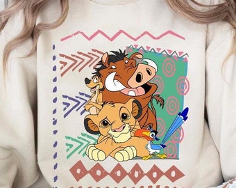 May include: A cream-colored sweatshirt featuring a colorful graphic of characters from The Lion King. The graphic includes Simba, Timon, Pumbaa, and Zazu, with tribal-inspired patterns in pink, green, and brown.