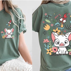 May include: Green t-shirt featuring a cartoon pig and rooster design with floral accents. The front of the shirt shows the pig and rooster with flowers. The back of the shirt has a larger version of the design.