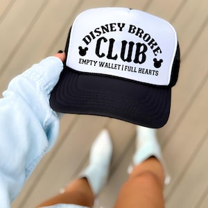 May include: Black and white trucker hat with the text "DISNEY BROKE CLUB" in a curved font. The hat also features the text "EMPTY WALLET | FULL HEARTS" and Mickey Mouse silhouettes. The hat has a black brim and mesh back.