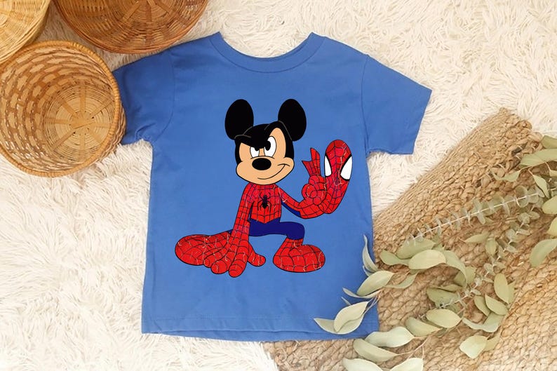 Op de afbeelding: Een blauw t-shirt met een stripfiguur die Mickey Mouse en Spider-Man combineert. Het personage draagt een Spider-Man-kostuum, met rode en blauwe kleuren. Het shirt ligt op een witte, zachte ondergrond.