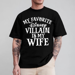 May include: Black t-shirt with the text "MY FAVORITE Disney VILLAIN IS MY WIFE" in white. The shirt has a crew neck and short sleeves. The text is in a stylized font.