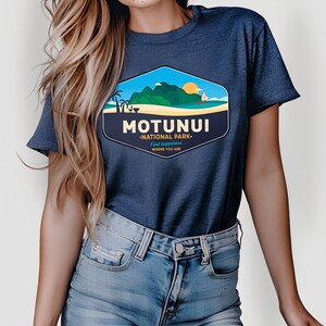 May include: Dark blue t-shirt with a graphic of a coastal scene and the words "MOTUNUI NATIONAL PARK". The design includes mountains, a beach, and a sunset. The shirt is made of a soft fabric, ideal for everyday wear.