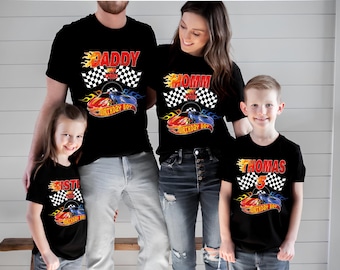 May include: A set of black t-shirts featuring a racing-themed graphic with a checkered flag, flames, and two race cars. The shirts display text including DADDY, MOMMY, SISTER, and THOMAS with the number 5, all styled with a vibrant red and orange font.