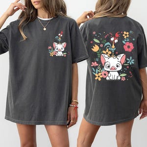 May include: Dark gray t-shirts with a cartoon pig and rooster design. The front of the shirt has a small graphic, while the back features a larger version with colorful flowers.