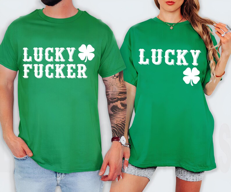 May include: Two green t-shirts with white text and a four-leaf clover design. One shirt says "LUCKY FUCKER" and the other says "LUCKY". The shirts are short-sleeved and worn by two people.