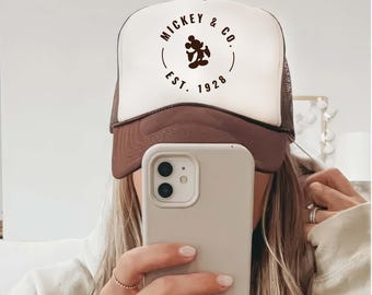 May include: A white and brown trucker hat with a brown Mickey Mouse silhouette and the text "Mickey & Co. Est. 1928" in a circle.