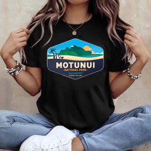 May include: Black t-shirt with a hexagonal graphic depicting a tropical island landscape. The graphic includes the text "MOTUNUI NATIONAL PARK" and "Find happiness where you are". The design features a beach, mountains, and a setting sun.